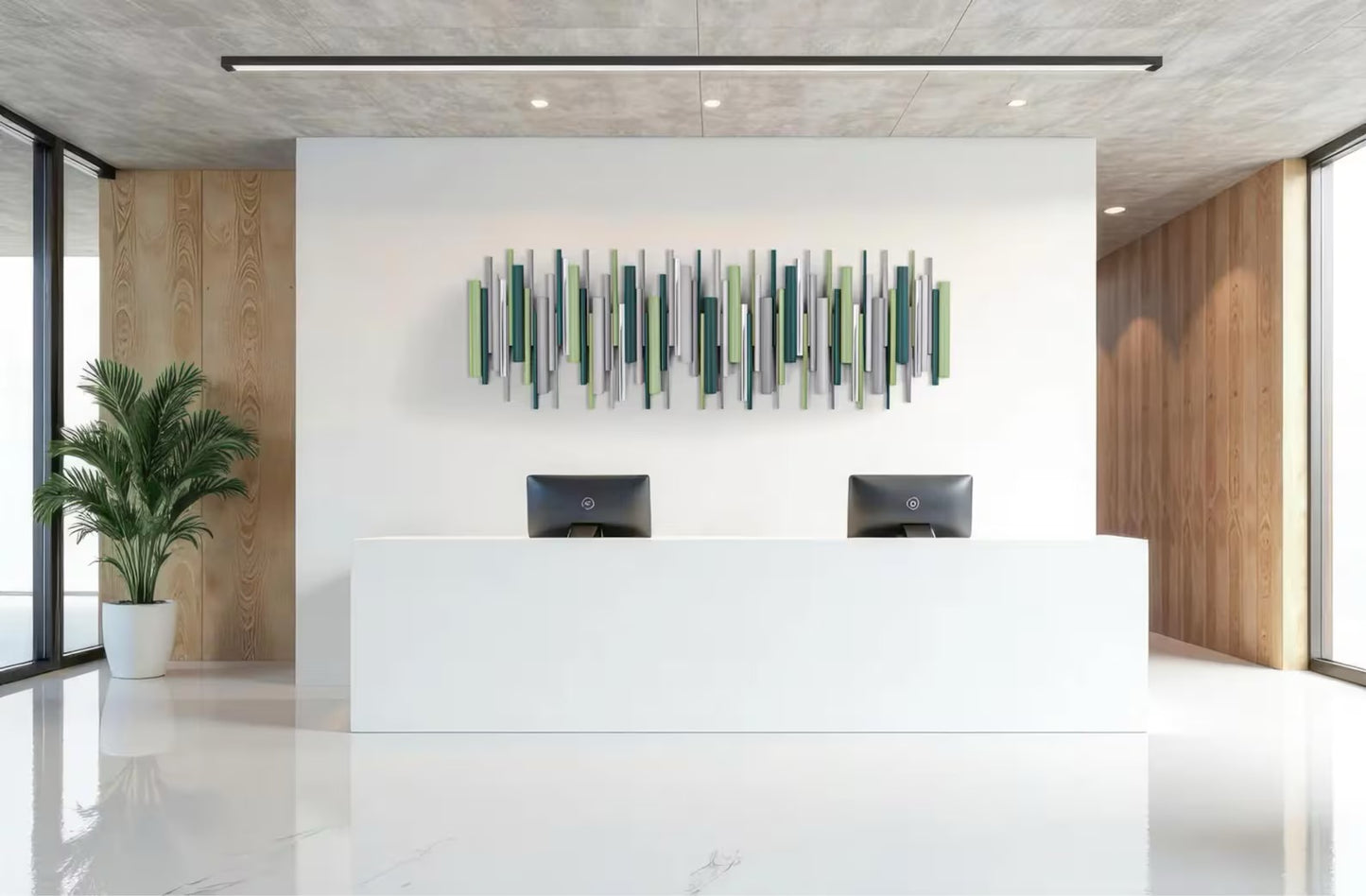 Modern reception desk in a bright office lobby with a white desk, two black computer monitors, a green potted plant, and a green and gray abstract wall art piece on a white wall.