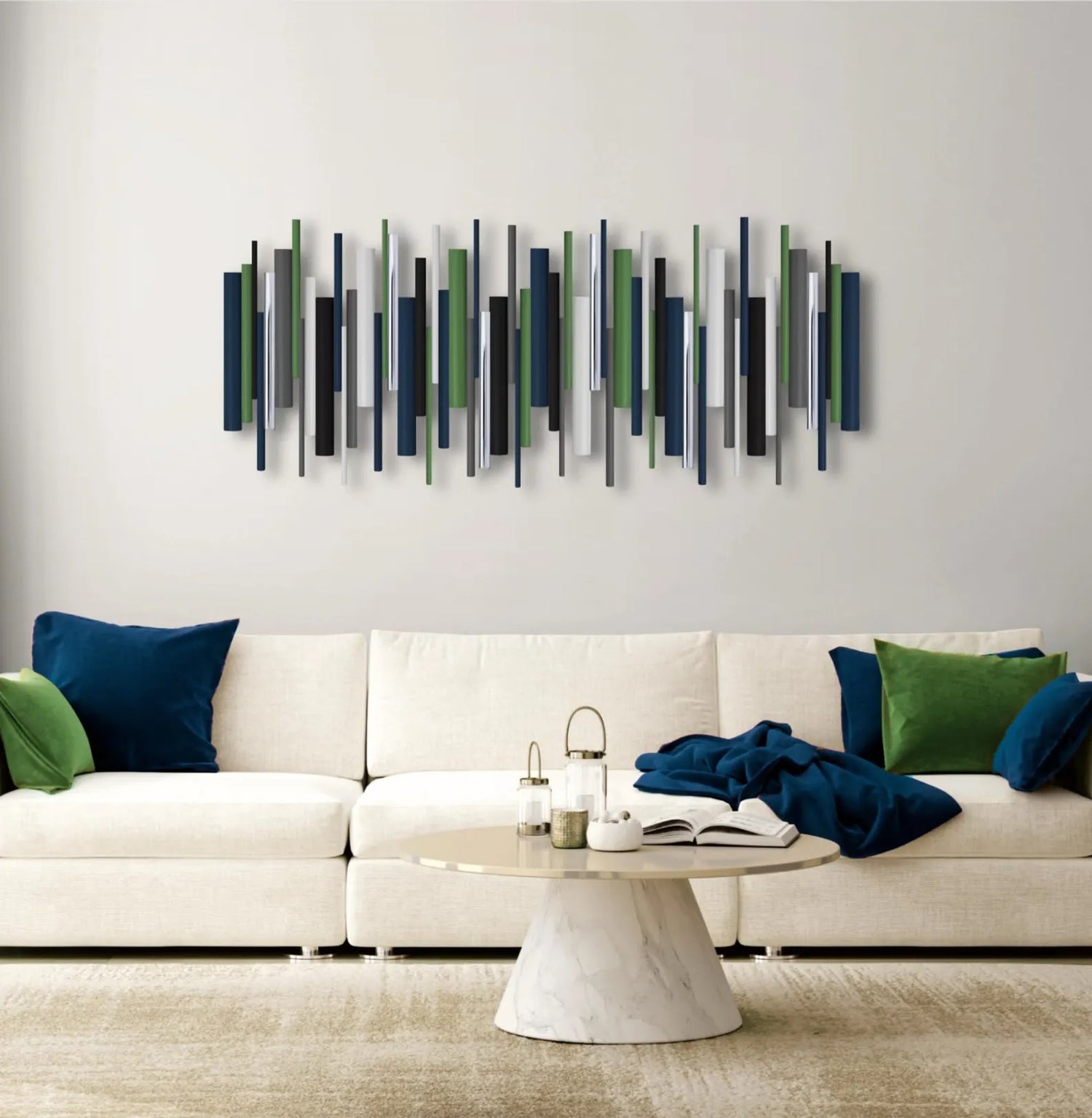 A modern wall art piece featuring vertical painted wooden dowels in navy, green, gray, and white, displayed above a white sectional sofa with blue and green pillows in a living room setting.