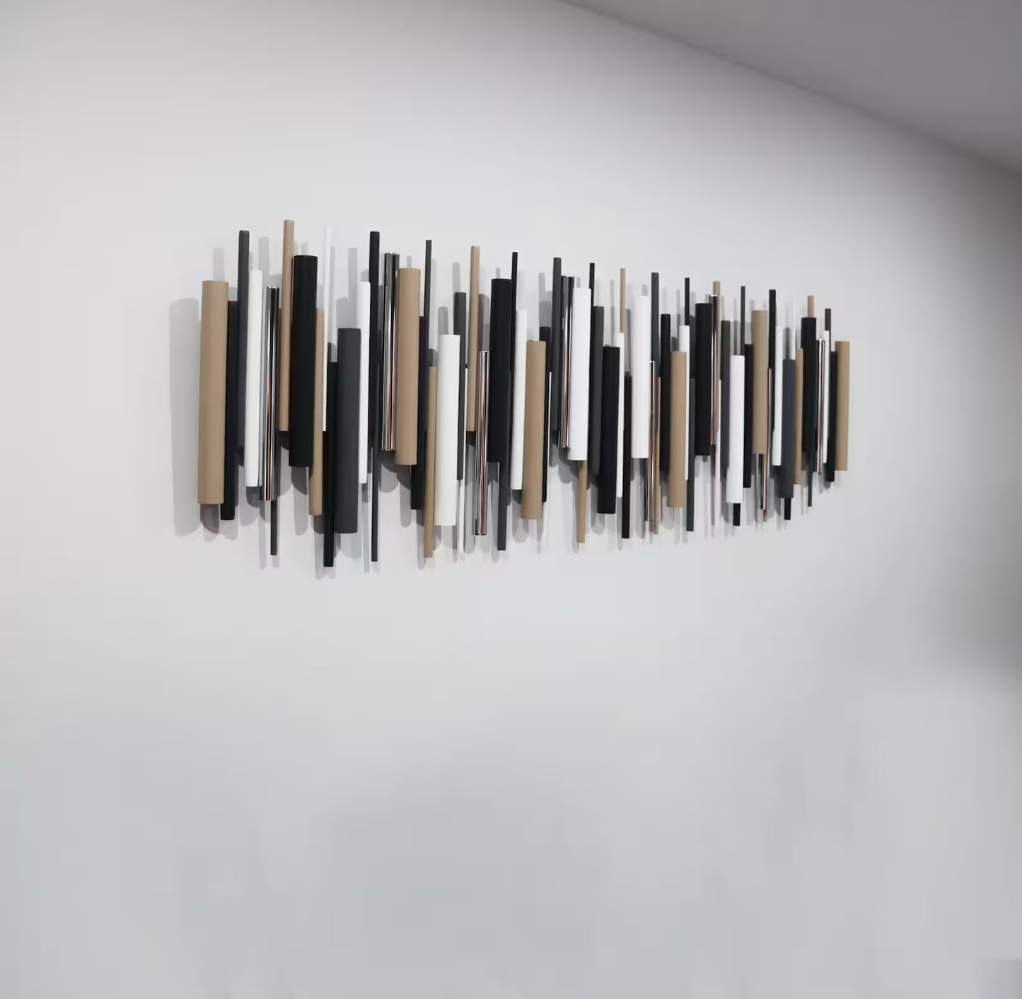 A modern wall art piece featuring a series of vertical rectangular rods in black, white, and natural wood tones, mounted on a plain white wall.
